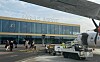 Ett flygplan står vid Aarhus Airport med markpersonal och servicefordon framför terminalbyggnaden.