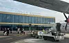 Ett flygplan står vid Aarhus Airport med markpersonal och servicefordon framför terminalbyggnaden.