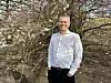 Person i vit skjorta står utomhus framför ett träd med vårblommor.