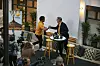 Två personer skakar hand vid ett podium framför fotografer och Ving-logga.