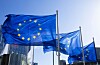EU-flaggor vajar framför glasbyggnader mot en klar blå himmel.
