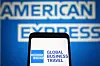 Smarttelefon som visar American Express Global Business Travel-logotyp framför American Express-skylt.