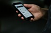 En hand håller en smartphone med en app öppen på skärmen mot en mörk bakgrund.