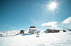 Skidområde med liftar, små byggnader och snöklädda backar under en klarblå himmel.