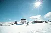 Skidområde med liftar, små byggnader och snöklädda backar under en klarblå himmel.
