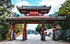Röd japansk tempelport med svart tak och stenlagd väg in mot ett öppet område.