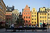 Ett torg med historiska, färgglada byggnader och människor som sitter på bänkar framför en staty.