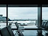 Ett Lufthansa-plan står parkerat vid en gate sedd genom terminalfönster med tomma stolar i förgrunden.
