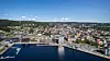 Flygvy över en kuststad med hamn, kajer, vatten och tätt bebyggt centrum.