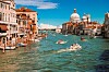 Båtar kör på en kanal i Venedig med historiska hus och en kyrkobyggnad i bakgrunden.