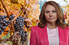 Druvor hänger på vinrankor i höstfärger bredvid en kvinna i rosa jacka.