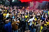 Stor folkmassa dansar och jublar i en lokal med röd belysning.
