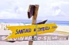 Gul vägskylt mot Santiago de Compostela vid en strand med havet bakom.