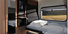 En sovkupé i ett tåg med bädd, mörka paneler, hylla och stort fönster mot landskap.