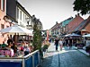 Människor går längs en kullerstensgata med marknadsstånd, parasoller och uteserveringar.