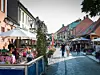 Människor går längs en kullerstensgata med marknadsstånd, parasoller och uteserveringar.