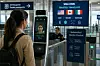 En resenär står framför en biometrisk passkontrollkiosk i en flygplatsterminal med informationsskyltar.