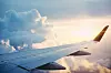 Utsikt från ett flygplansfönster över en vinge, moln och solnedgång.