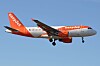 Ett orangevitt Easyjet-flygplan flyger lågt mot en blå himmel med landningsställ nedfällt.