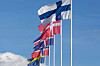 Alla de nordiska flaggorna från Finland, Danmark, Island, Norge och Sverige vajar på höga master mot blå himmel och moln.