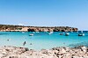 Turkos vik med flera små båtar, badande personer och en stenig strand under klarblå himmel på Mallorca.
