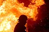 Siluett av brandman framför kraftiga lågor och flygande gnistor i en skogsbrand.