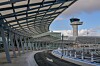 En modern flygplats med glasöverbyggnad, tom väg och ett kontrolltorn i bakgrunden under klar himmel.