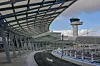 En modern flygplats med glasöverbyggnad, tom väg och ett kontrolltorn i bakgrunden under klar himmel.