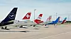 Flera passagerarflygplan står parkerade på flygplatsens platta med olika flygbolagslogotyper på stjärtfenorna.