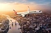Ett Qantas-målat passagerarplan flyger över en stad med flod, broar och solnedgång i bakgrunden.
