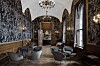 En hotellounge med mörka väggar, valv, kristallkrona, bord och fåtöljer samt stora fönster.