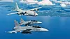 Tre gråa stridsflygplan flyger tätt i formation ovanför hav och kust.