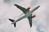 Ett vit- och orangefärgat passagerarflygplan med uppfälld landningsställ mot en grå himmel.