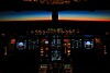Flygplanscockpit med upplysta instrument och mörk himmel med färgad horisont utanför framrutan.