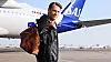 En man med brun väska står framför ett SAS-flygplan på flygplatsen.