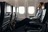 En passagerare sitter lutad tillbaka i ett flygplanssäte vid ett fönster med skärm framför sig.