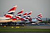 Flera British Airways-flygplan står på rad vid en flygplats med landningsbanor i förgrunden.