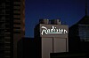 Belyst Radisson-skylt på en hotellbyggnad mot en mörk kvällshimmel.