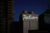 Belyst Radisson-skylt på en hotellbyggnad mot en mörk kvällshimmel.