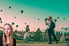 Kvinna i förgrunden och resenär med kamera i ett landskap med luftballonger.