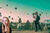 Kvinna i förgrunden och resenär med kamera i ett landskap med luftballonger.