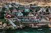 Färgglad kustby med trähus, bryggor och små båtar nedanför en brant klippa.
