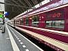 Ett vinrött European Sleeper-tåg står vid en täckt perrong med spår och stationsskyltar.