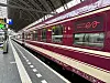 Ett vinrött European Sleeper-tåg står vid en täckt perrong med spår och stationsskyltar.