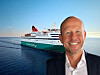 Leende man i kostym framför ett passagerarfartyg på havet.