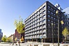 Hög mörk hotellbyggnad vid ett torg i centrala Stockholm, omgiven av träd, gator och gångtrafikanter.