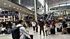 Resenärer med bagage rör sig genom en ljus och välbesökt flygplatsterminal.