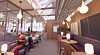 Modern lounge med sittplatser, bord, lampor och en person vid ett fönster.