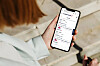 Person i ljus jacka håller en smartphone med en lista över reseinformation.