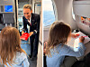 Ett barn ritar vid flygplansfönstret medan en kabinanställd räcker fram ett rött paket.
